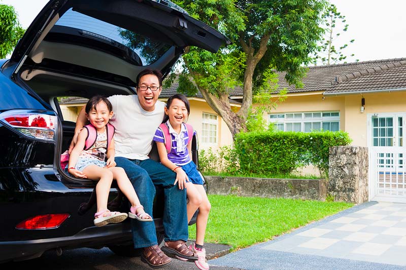 Family sitting on back of car in front of house